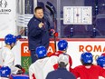Laval Rocket head coach Jean-François Houle, on his skates next to a hockey diagram affixed to the glass, addresses players on his team who are kneeling in front of him during practice at the Place Bell Sports Complex in Laval.