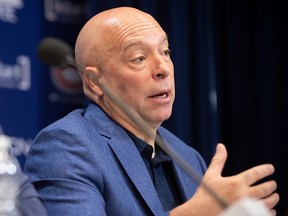Canadiens general manager Kent Hughes, wearing a blue jacket over a black shirt, is seen gesturing with his right hand during a news conference.