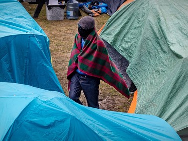 A person has a plaid blanket wrapped around shoulders while walking among tents