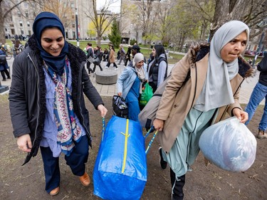 Two women wearing headscarves, one of them smiling, carry a full bag through a university campus