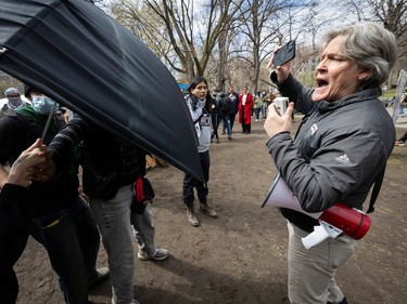 A man holding a megaphone in one hand and a cellphone in another yells at people using an umbrella to block his view