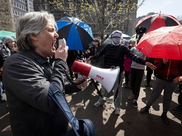 A man yells into a megaphone while people stand in the background, some holding open umbrellas