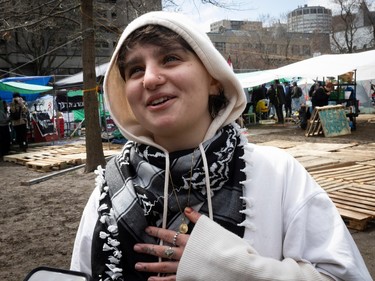Ari Nahman, wearing a kaffiyeh and a hoodie, stands outside an encampment