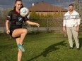 A girl plays soccer with her dad in the background