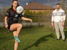 A girl plays soccer with her dad in the background