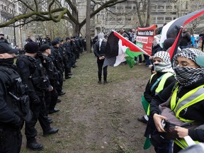 Police officers in tactical gear line up facing pro-Palestinian protesters on the grass