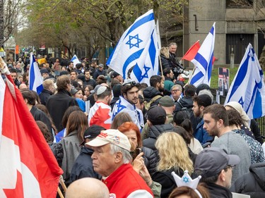 A large group of people, many holding Israel and Canada flags, gather on a sidewalk