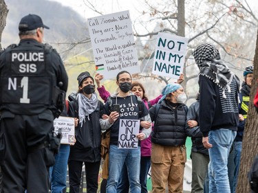 A police officer stands watch in front of a group of protesters, one carrying a sign reading 'Not in my name'