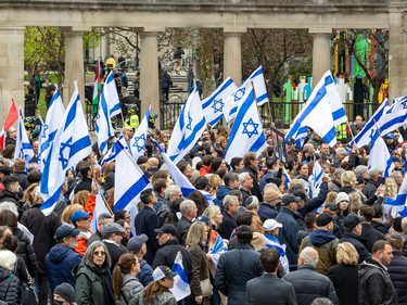 A large group of people carrying Israeli flags stands outside a large stone pillared gate