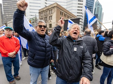 Two men yell while holding one arm in the air, with Israeli flags in the background