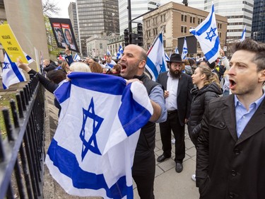 A man holds up an Israeli flag while he and another man yell something