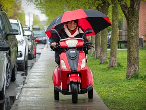 A woman on a red motorized wheelchair is holding a large red and black umbrella.