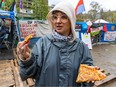 Ari Nahman, wearing a rain jacket and hoodie, holds two slices of pizza while speaking outside an encampment