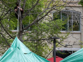 A masked man in a treet pulls on a rope attached to a large green tarp