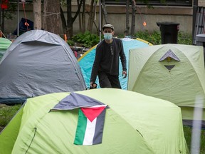 A protester walks between tents. One of the tents has a Palestinian flag on it.