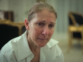 Céline Dion, wearing a white collared shirt, cries as she looks off to the side while sitting in a room