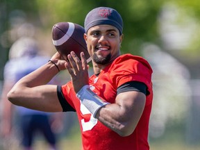 Alouettes QB Caleb Evans, in a red jersey, holds the football behind his head as he prepares to throw during a practice.