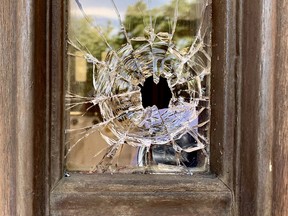 Closeup of a bullet hole in a window, framed in wood. Trees are reflected in the broken glass.