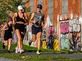 Runners jog past graffiti on an urban street.