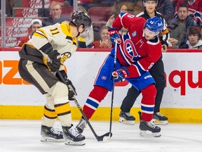 Canadiens' Joshua Roy, right in Habs' red jersey, and Bruins' Trent Frederic compete for the puck with their sticks.