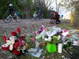 Cyclists bike past a makeshift shrine of flowers and candles.