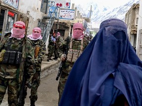 Taliban security personnel stand guard as a burqa-clad woman walks along a street at a market in the Baharak in February. The Taliban returned to power in Afghanistan in 2021.