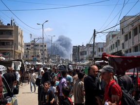 Palestinians crowd a street as smoke rises near Israeli strikes in Rafah, southern Gaza Strip, May 7, 2024.