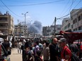 Palestinians crowd a street as smoke billows nearby from Israeli strikes in Rafah in the southern Gaza Strip on May 7, 2024.