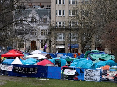 Dozens of tents are visible on a grassy field surrounded by a fence with banners and tarps attached to it