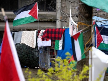 Palestinian flags and blankets are draped over a temporary fence, while another Palestinian flag hangs above on a post