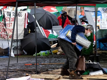 A person bends over to pick something up underneath a temporary shelter, with open umbrellas and banners in the background