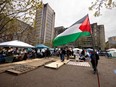 A large Palestinian flag waves in front of an encampment on the McGill campus with a large tower in the background