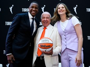 Three people gather around a basketball smiling for cameras with a backdrop that shows the WNBA logo and the word Toronto behind them