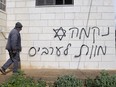 A man looks at graffiti that reads, in Hebrew, "revenge, death to Arabs," allegedly sprayed by Jewish West Bank settlers in the Palestinian West Bank village of Turmus Ayya, Sunday, Feb. 18, 2024.