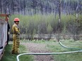 A firefighter monitors a wildfire sprinkler hose in the evacuated neighbourhood of Grayling Terrace in Fort McMurray, Alta., Thursday, May 16, 2024.