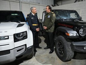 Two men in police uniforms talk to each other while standing between two large vehicles.