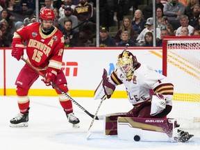Boston College goaltender Jacob Fowler, in white jersey and burgundy pants, makes a save in the butterfly position with the puck outside his left pad as Denver forward Carter King, left, closes in for a rebound.