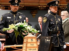 Two officers in uniform hold a flower wreath near a table with the date marked on it in the Blue Room of the National Assembly