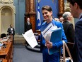 Geneviève Guilbault smiles as she holds papers including the printout of a bill while standing in the centre of the Blue Room at the National Assembly