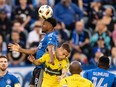 CF Montréal midfielder Rida Zouhir, wearing the team's blue jersey, is seen heading the ball at the top of his jump, while holding off Columbus Crew defender Yevhen Cheberko, in yellow, with his left arm.