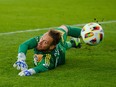 A goalkeeper extended on the ground looks behind him as a ball passes him by