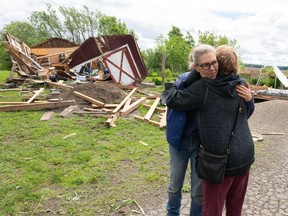 Two women hug with wreckage from a destroyed building behind them
