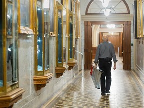 A man is seen from behind walked along an elegant hallway with a ladder in his hand.