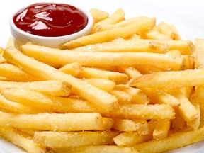 A plate of golden french fries is seen with a small container with ketchup in the top left of the frame.