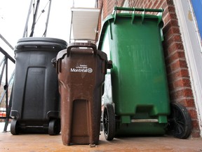 A compost container sits between a garbage can and a recycling bin on the balcony of a house in Montreal.