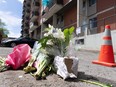 Flowers are left on the asphalt of an alleyway after a triple homicide. An orange cone is in the background, next to a building.