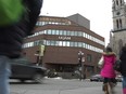 A low angle shot shows an intersection with pedestrians and traffic crossing, and a brown building with a UQAM logo on it at the opposite corner
