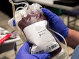A pair of gloved hands hold a blood bag at a clinic