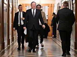 Quebec Premier François Legault walks down a corridor to a news conference.