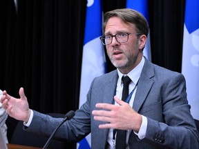 French language commissioner Benoît Dubreuil gestures and speaks during a news conference. Quebec flags are seen in the background.